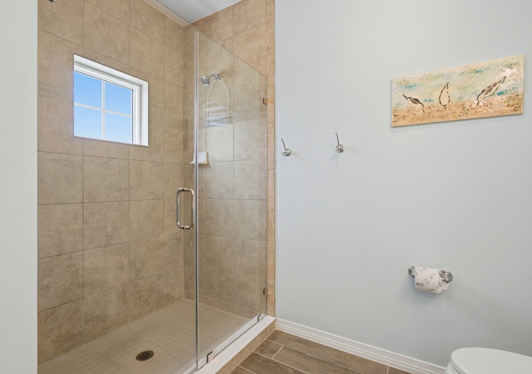 Step into your private spa-like retreat with a spacious glass-enclosed shower featuring warm neutral tones and coastal charm—perfect for unwinding after a day of exploration.
