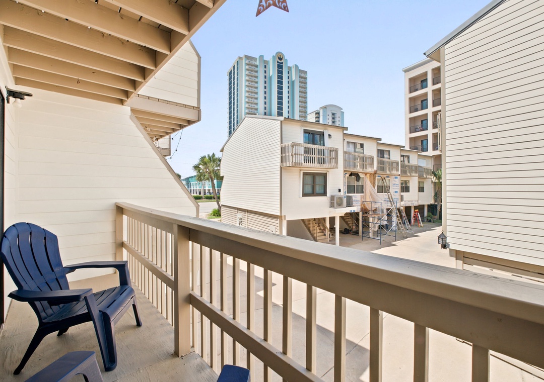 The balcony features a coastal neighborhood view with palm trees and beachside architecture, just steps from the sand and nearby high-rise landmarks.