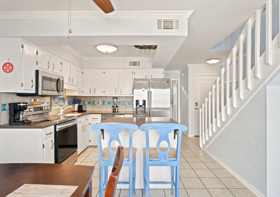 Your bright, fully-equipped kitchen invites you to whip up morning coffee or a family meal. Notice the island seating, stainless appliances, and cheerful coastal touches that make this space feel both practical and welcoming.