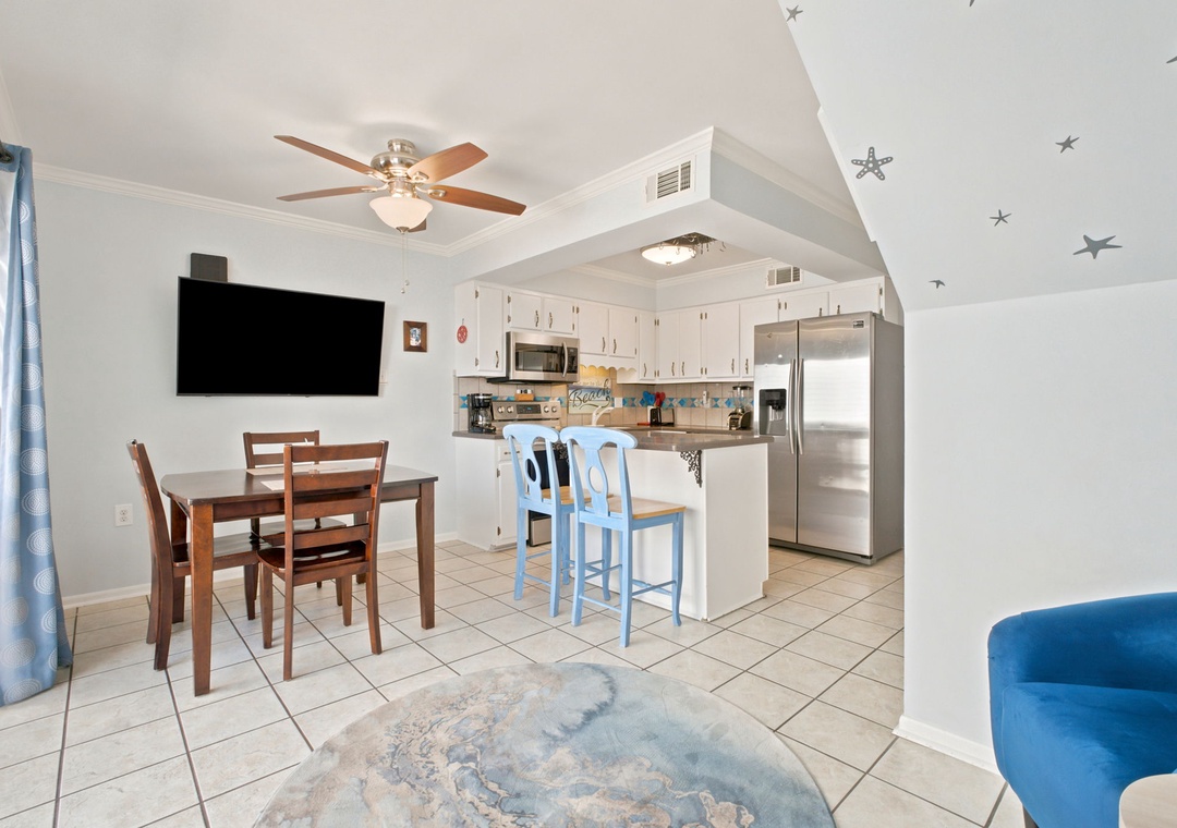 Step into an inviting open-concept space where coastal charm meets comfort—warm wood dining, breezy blue accents, and a fully-equipped kitchen ready for your beachside meals.