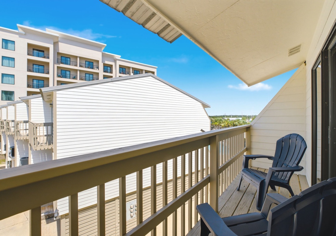 A covered balcony with seating overlooks nearby buildings and a clear blue coastal sky.