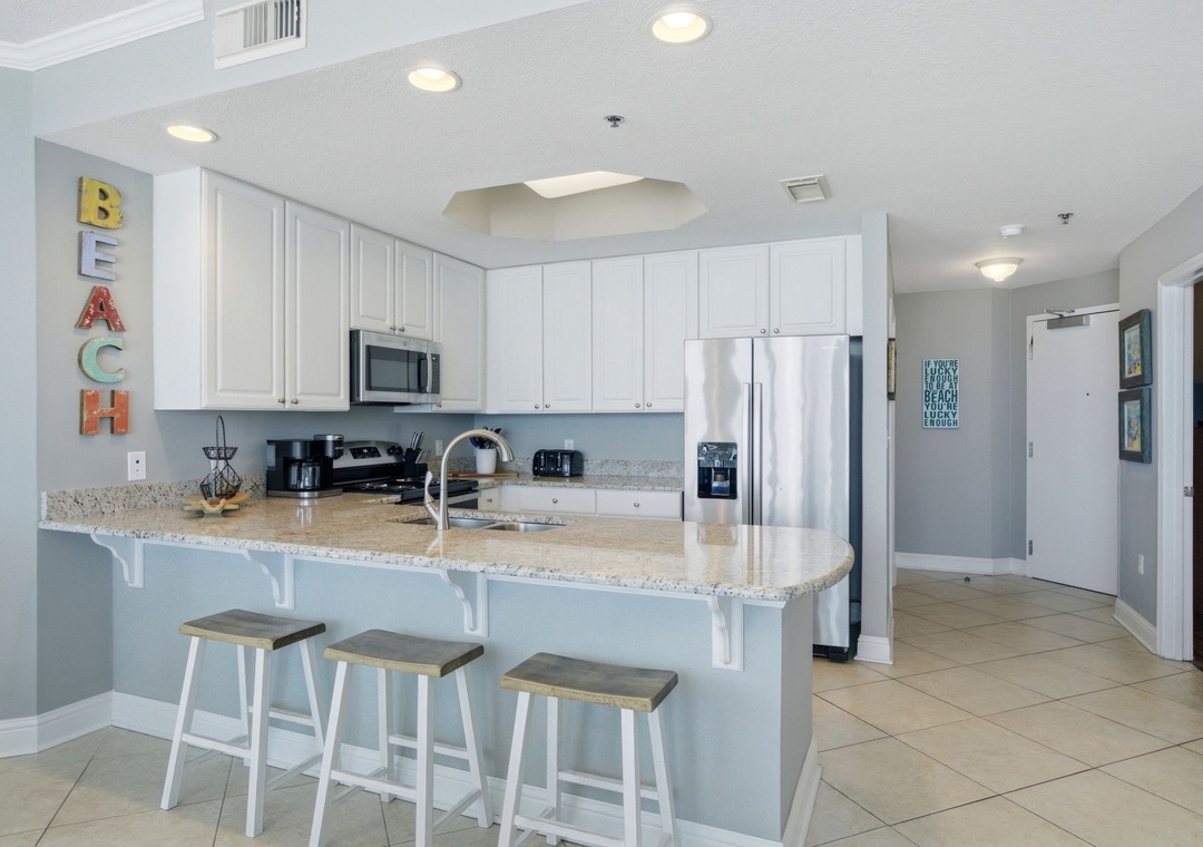 Lighthouse 418- Your bright, beach-themed kitchen awaits with a spacious breakfast bar for casual dining, modern appliances, and soft coastal colors that invite you to relax and enjoy your vacation meals.