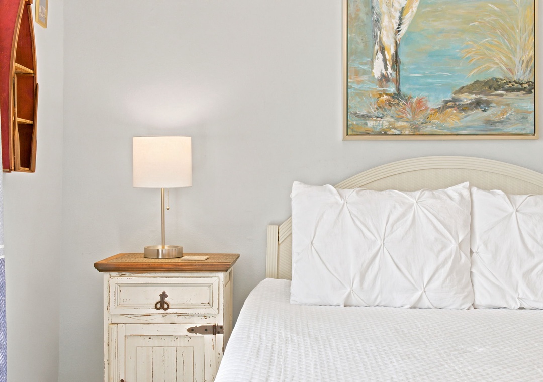 Sink into plush white linens and enjoy soothing coastal artwork above your bed. Soft bedside lighting sets the perfect mood for relaxation.
