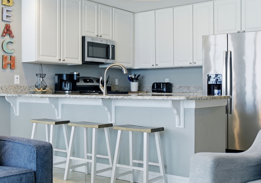 Lighthouse 418- Your bright, fully equipped kitchen features stainless appliances, a breakfast bar with stools, and a cheerful coastal vibe that makes morning coffee and meal prep feel effortless and inviting.