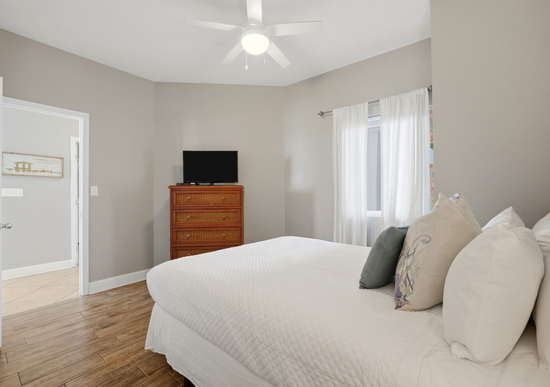 Lighthouse 418- Unwind in your serene bedroom, featuring a plush bed, ceiling fan, TV, and warm hardwood floors—your perfect retreat after a day of adventure.
