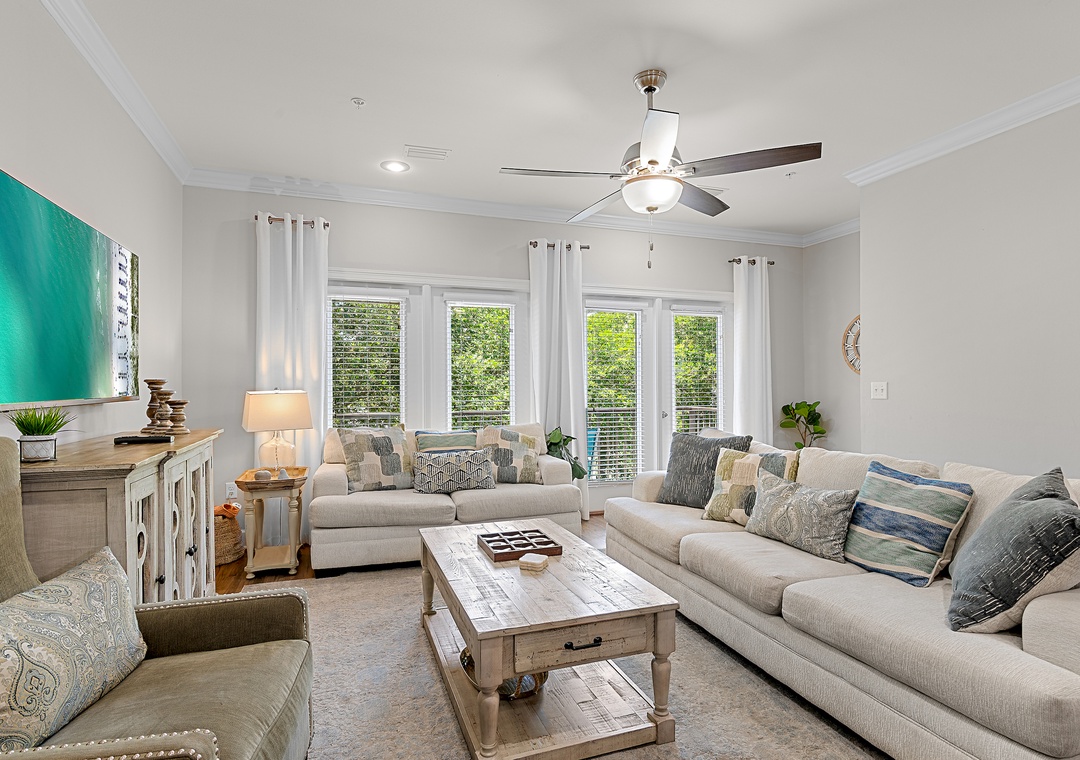Bright, airy living room with coastal decor, oversized sectional, large windows, and a smart TV — the perfect place to unwind together.