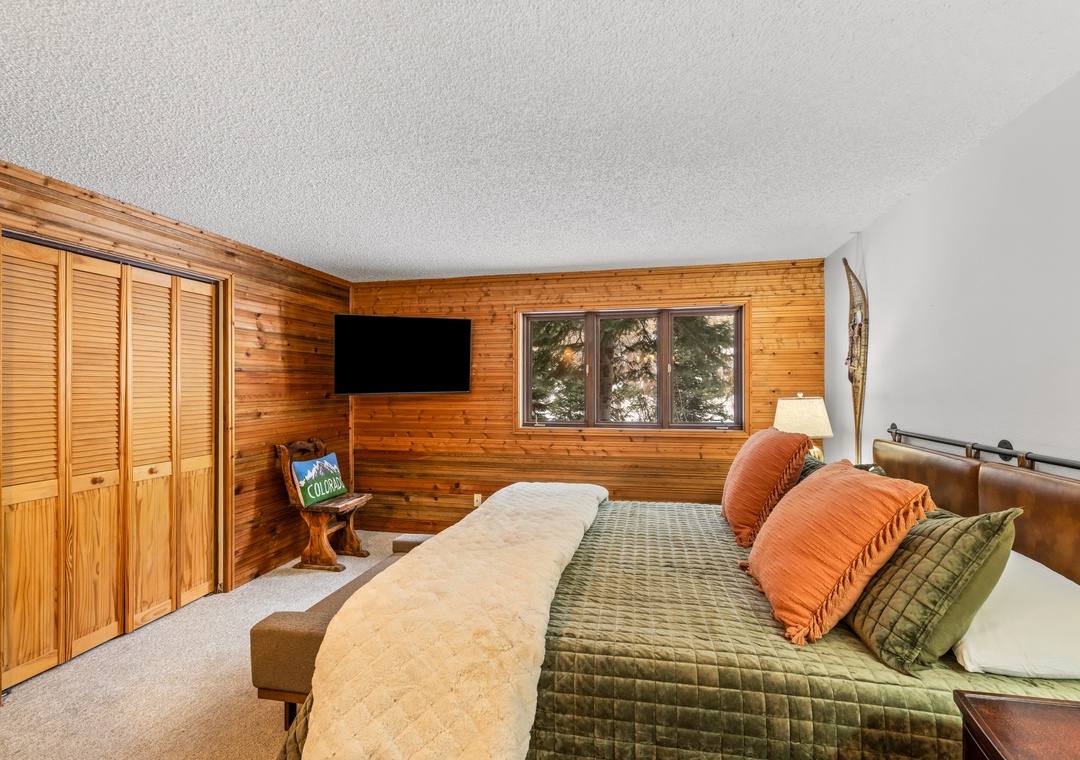 Relax in your cozy primary bedroom with warm wood accents, plush bedding, and peaceful forest views through your window.