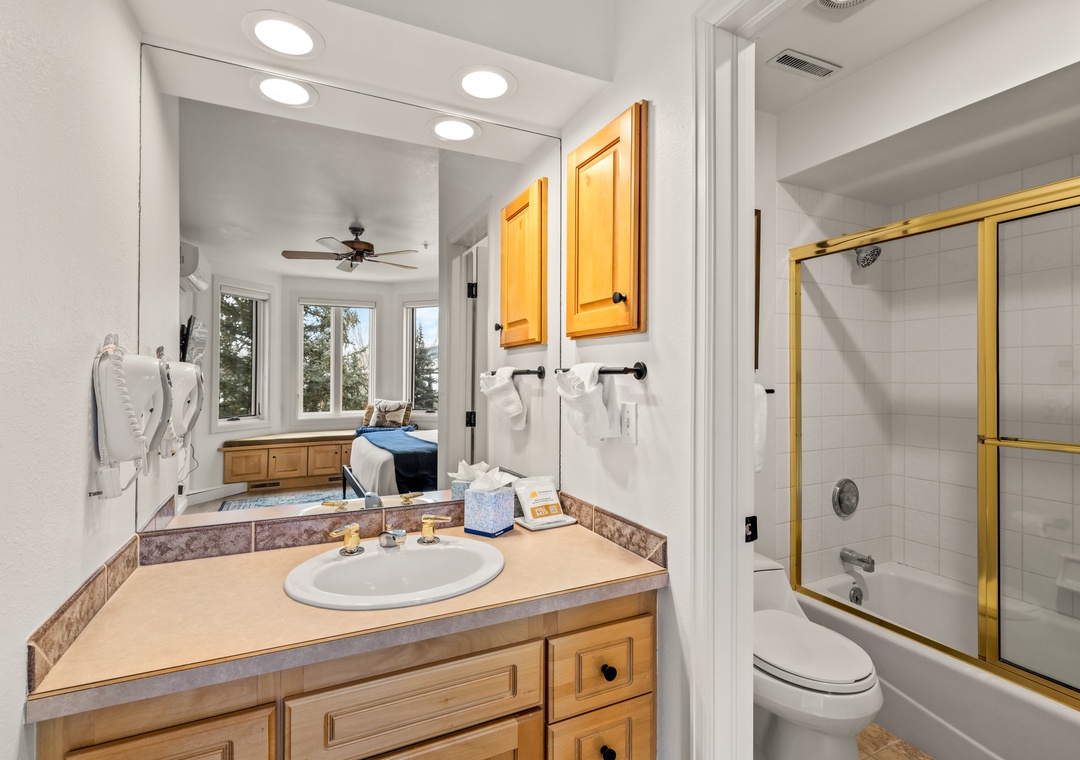 Your private bathroom features warm wood cabinetry, spacious vanity, and a relaxing tub-shower combo with elegant glass doors.