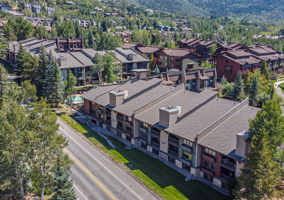 An aerial view captures the property nestled in a mountain community, surrounded by forested hillsides and neighboring residences.