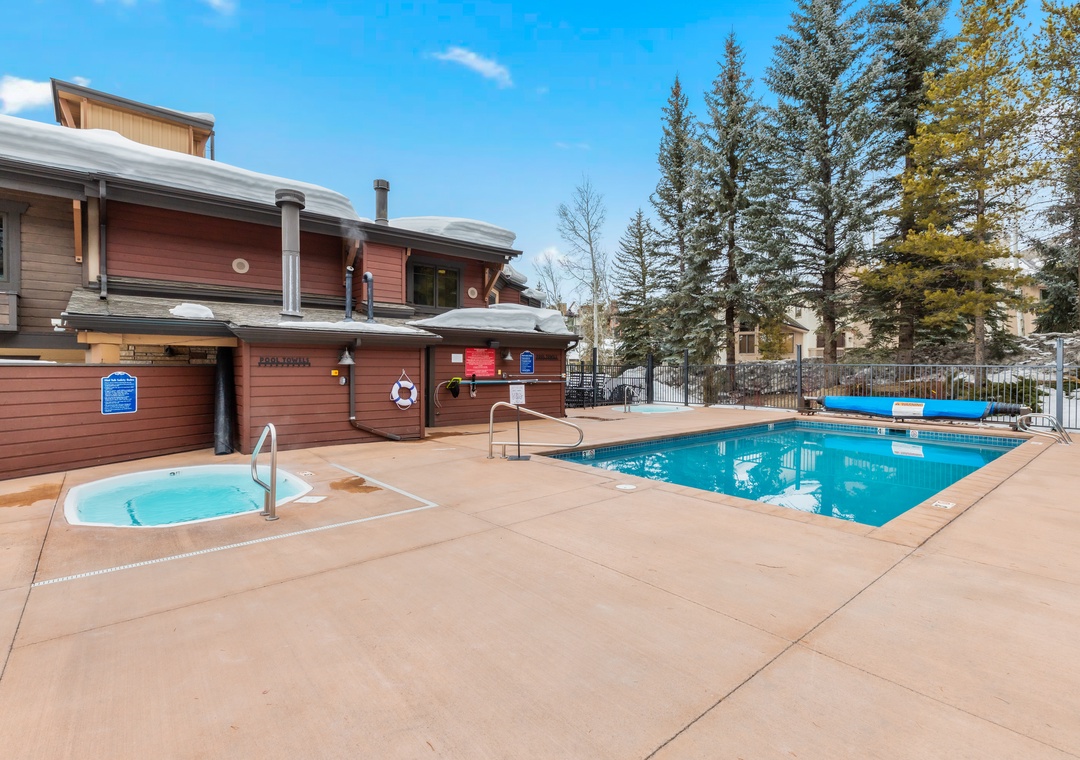 Outdoor pool and hot tub area with a rustic wooden clubhouse, surrounded by tall evergreens and crisp mountain air—perfect for refreshing after a day of adventure.