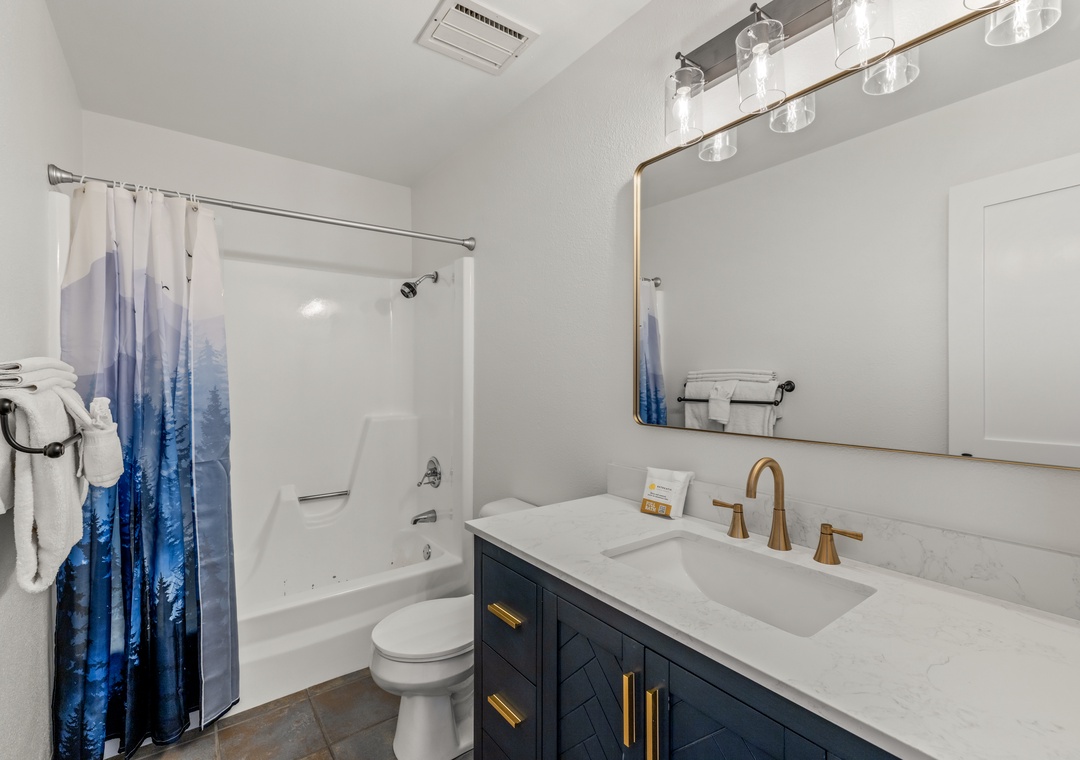 Refresh in your elegant upstairs bathroom featuring modern navy cabinetry, and a relaxing tub-shower combo with mountain-inspired artwork.