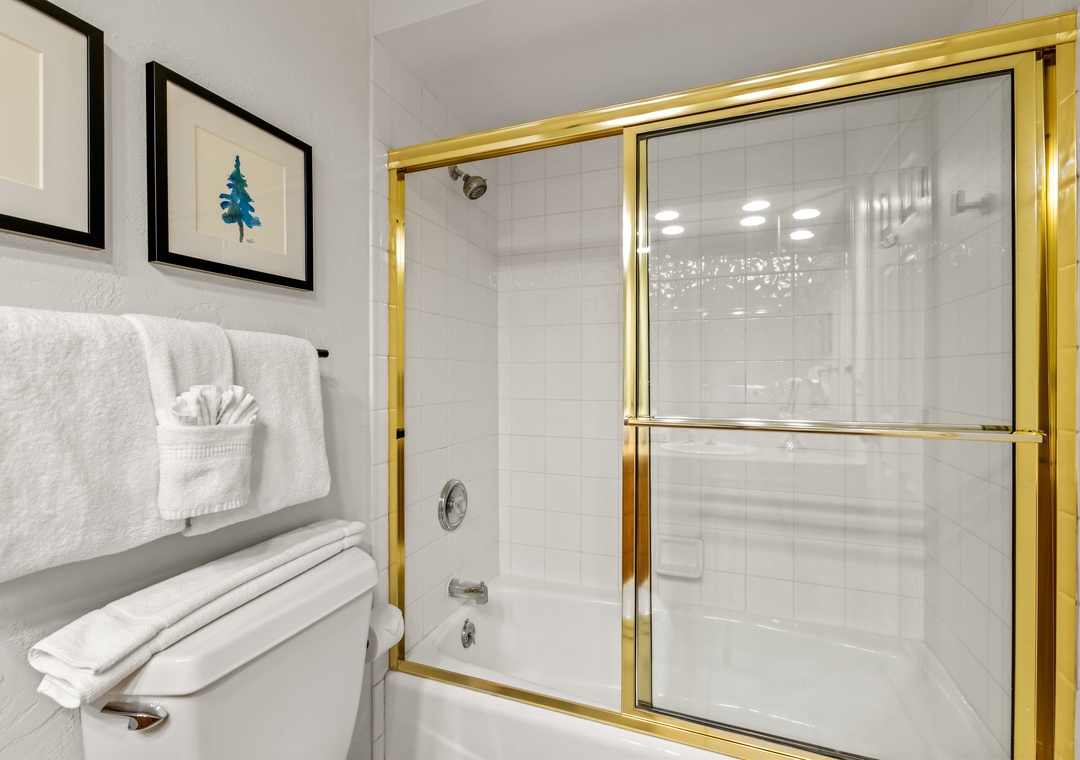 Unwind in your elegant bathroom featuring a gleaming tub-shower combo with gold accents and fresh white towels waiting for you.