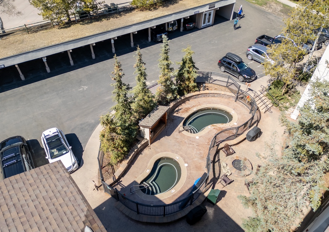 Aerial view showcasing the property's dual hot tub area, surrounded by parking and mature trees—a relaxing outdoor retreat for guests.