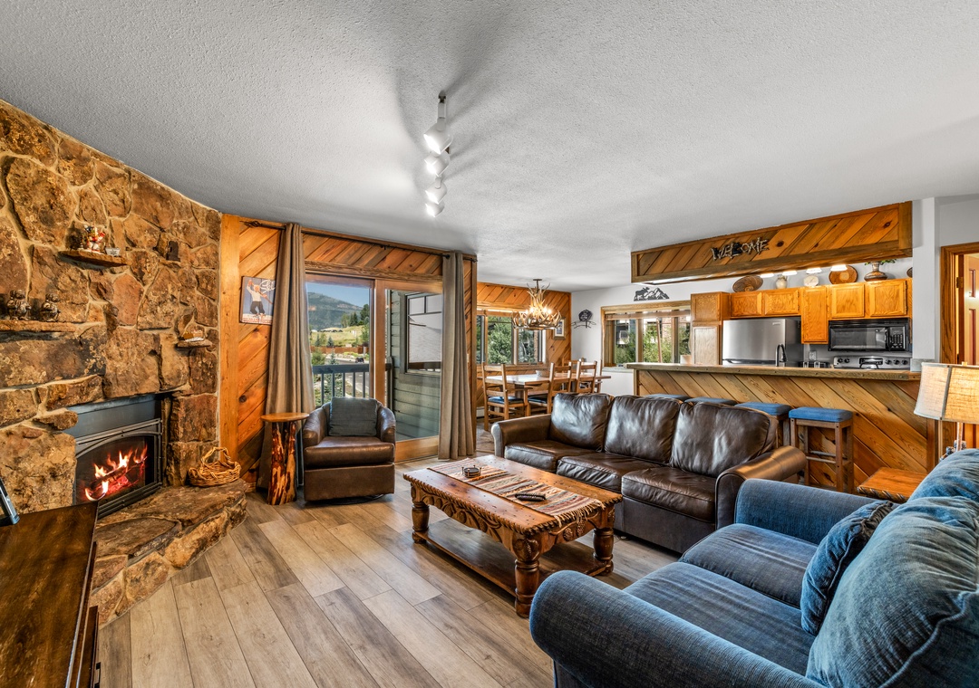 Unwind in your spacious living area with rustic stone fireplace and handcrafted furnishings. The open layout connects you to mountain views through the balcony door and a welcoming kitchen perfect for cozy gatherings.