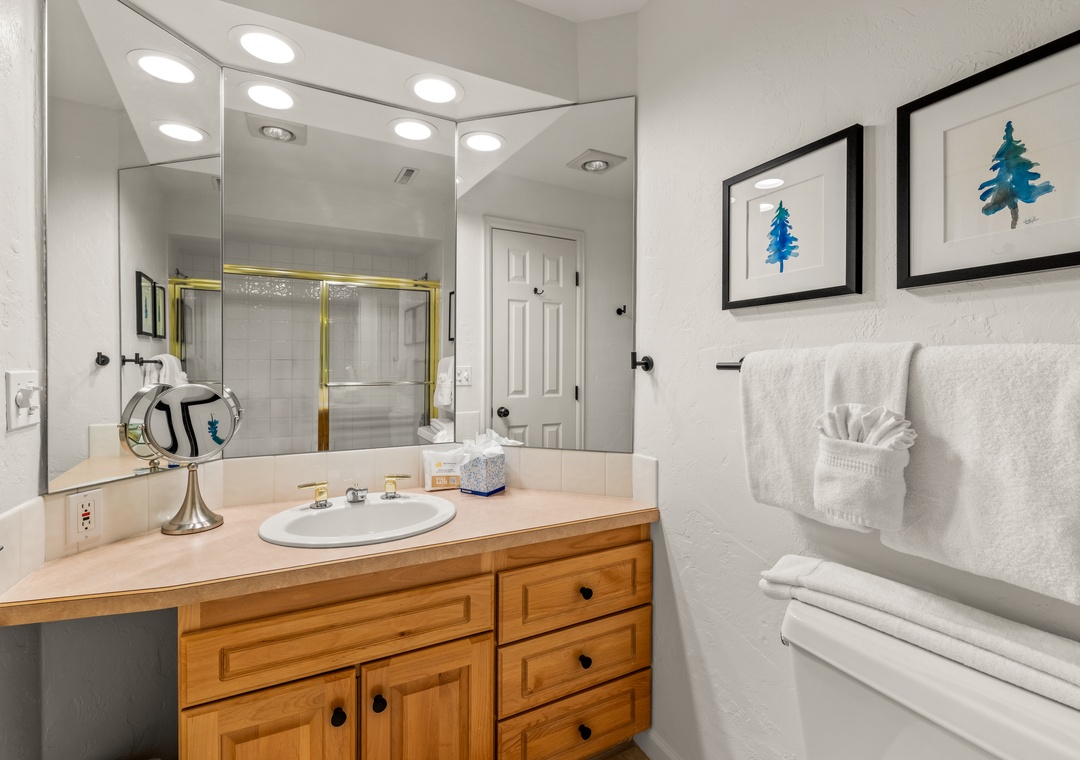 Your spacious bathroom features warm wood vanity, bright recessed lighting, and fluffy towels ready for your relaxing soak.