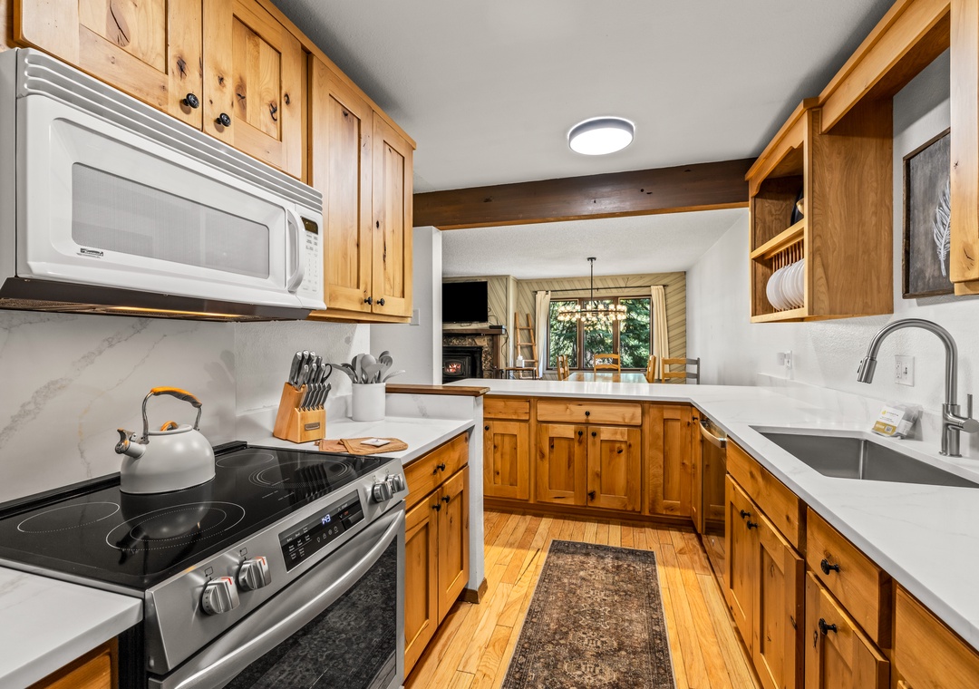Prepare meals in your fully equipped kitchen with warm wood cabinetry, modern appliances, and bright natural light streaming through windows overlooking the adjacent living space.