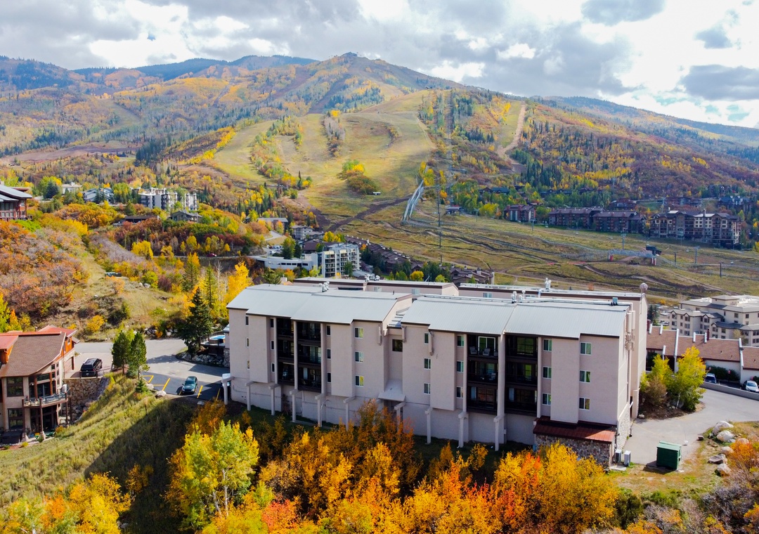 Aerial view of the property nestled in a mountain valley during autumn, with ski slopes and colorful fall foliage blanketing the surrounding hillsides.