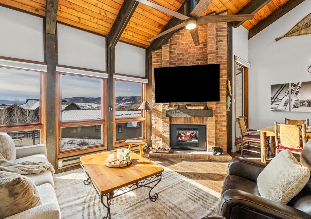 Cozy up by your crackling fireplace while soaking in breathtaking mountain vistas through floor-to-ceiling windows in this rustic-chic living space.