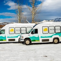 Two branded shuttle vans ready for guest transportation against a scenic mountain backdrop. Perfect for hassle-free transfers to nearby attractions or exploring the area in comfort.