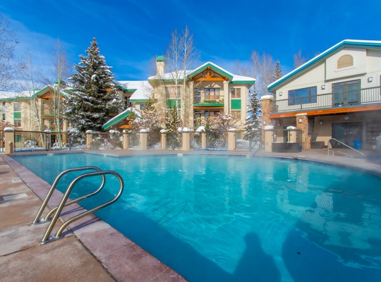 A sparkling outdoor pool set against snow-dusted evergreens and mountain air—your perfect winter escape awaits.