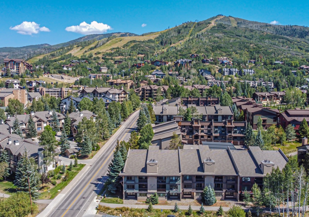 Aerial view of a mountain resort community nestled among evergreen trees and rolling peaks, with ski slopes visible in the distance.