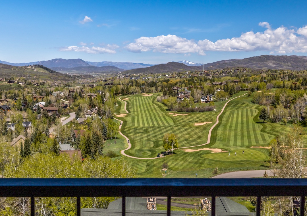 The property sits above pristine golf fairways with mountain peaks rising in the distance, surrounded by lush valley scenery and tree-lined residential areas.