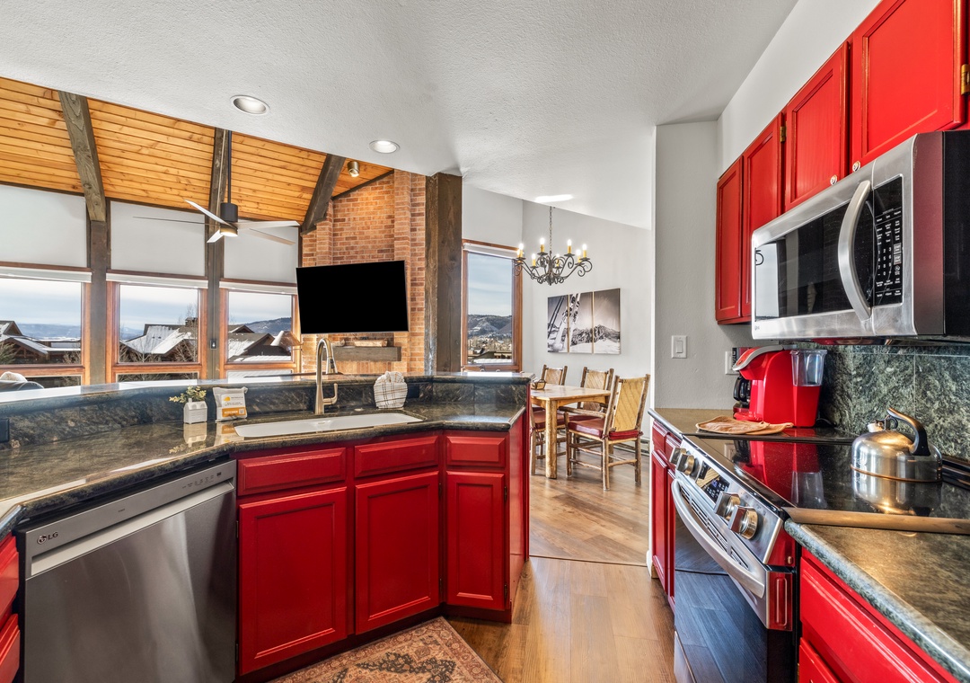 Your fully-equipped kitchen features vibrant red cabinets, granite counters, and stainless appliances—perfect for preparing meals while enjoying mountain views.
