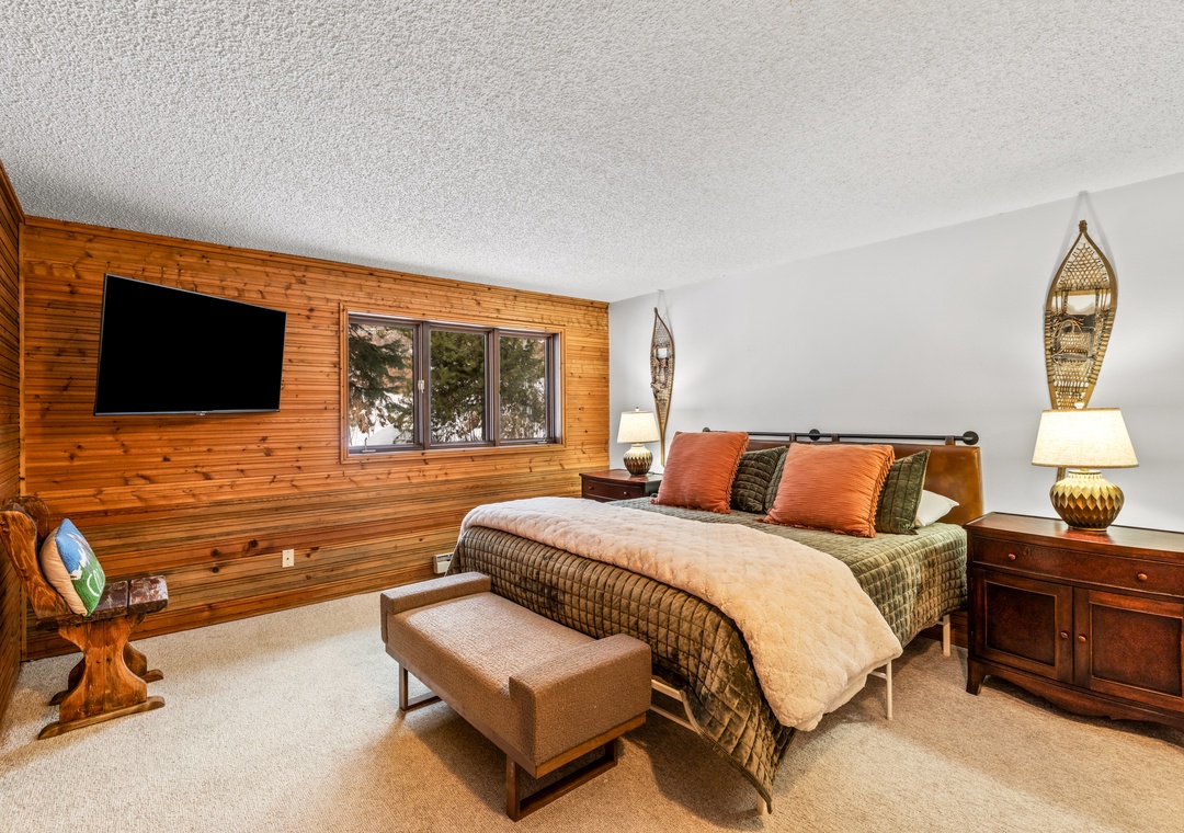 Unwind in your cozy primary bedroom featuring warm wood paneling, plush bedding, and modern amenities for the perfect mountain retreat.