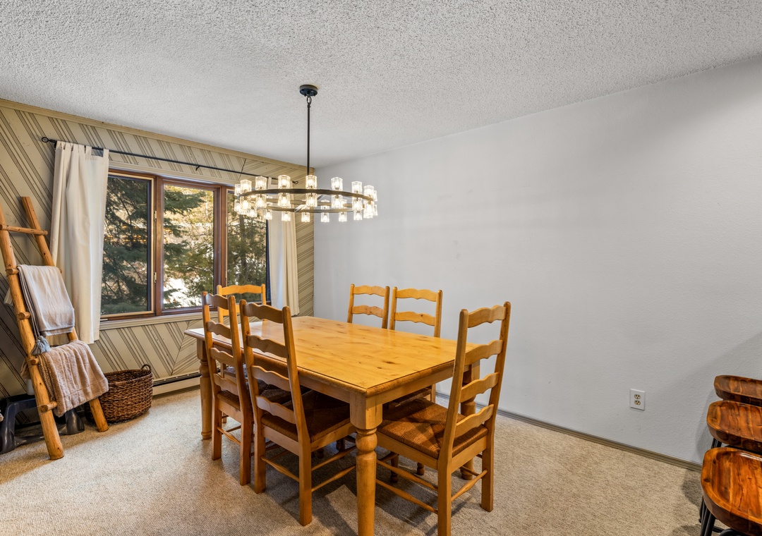 The dining area offers a rustic table, warm wood finishes, and plenty of natural light overlooking the trees.