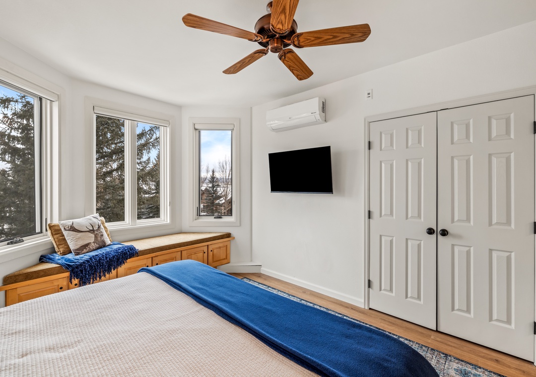Unwind in your bright bedroom featuring a cozy window bench, wall-mounted TV, ceiling fan, and built-in storage for complete comfort.