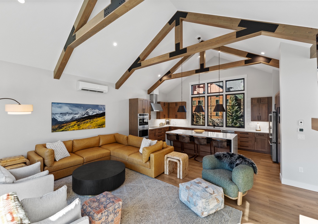 Relax in your open-concept living space with soaring wood beams, modern kitchen, and mountain artwork creating the perfect alpine retreat atmosphere.