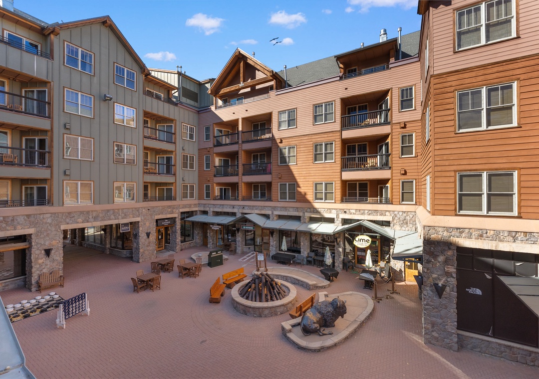 This mountain resort features multi-story buildings surrounding a central courtyard with fire pit seating and retail shops at ground level.
