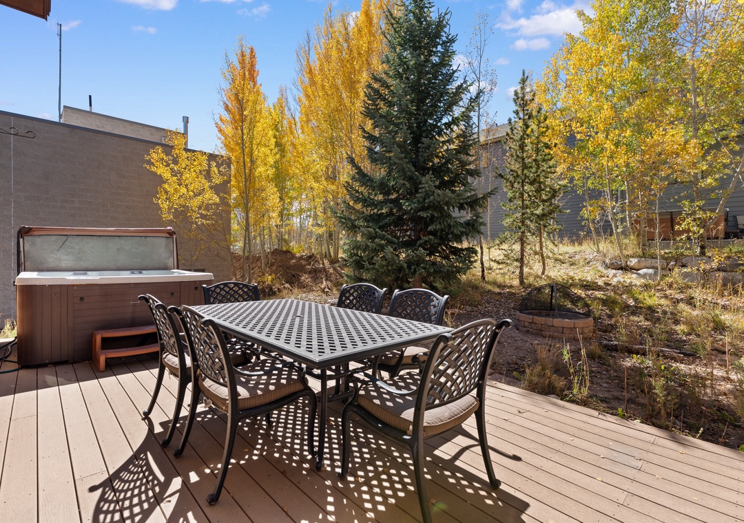 A wooden deck with dining table for six and hot tub, surrounded by golden aspens and evergreens under blue skies—perfect for crisp mornings or peaceful autumn evenings.