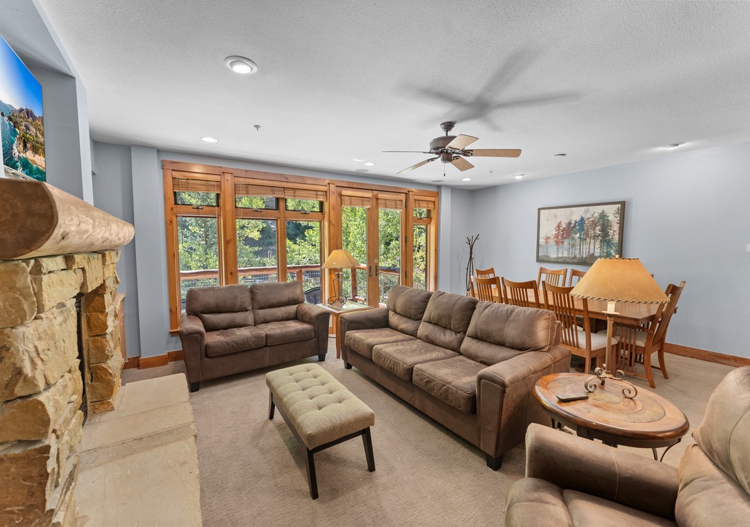 Relax in your spacious living area with plush leather seating, stone fireplace, and windows overlooking lush greenery.