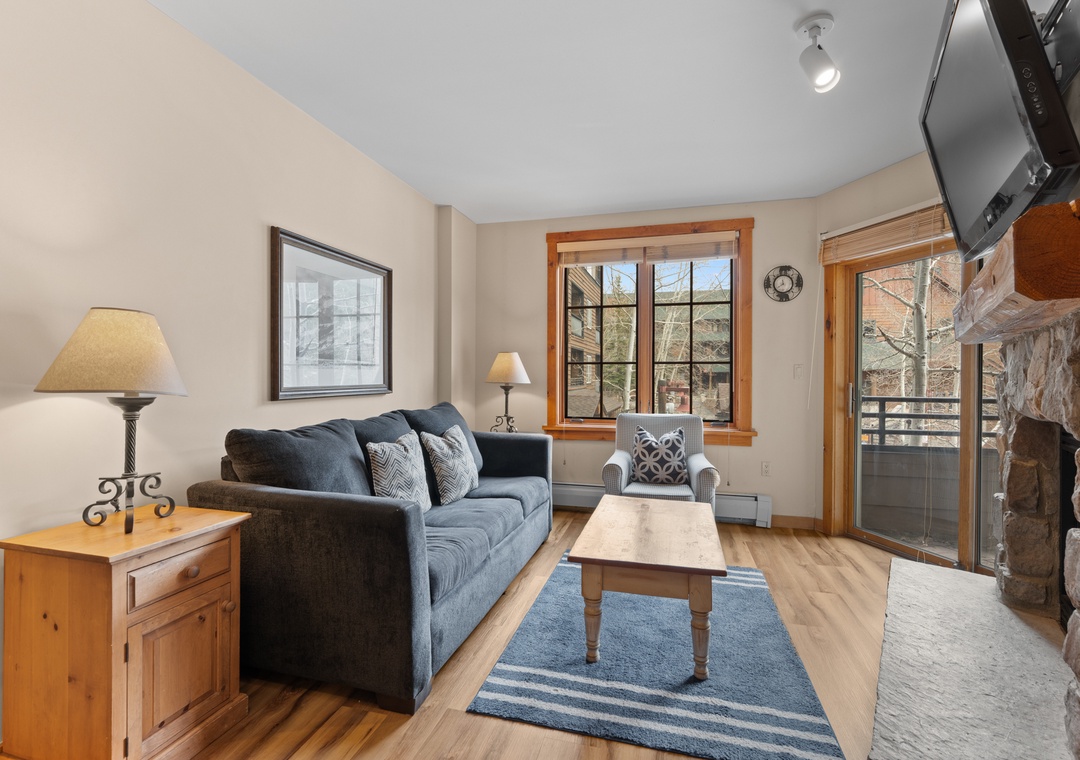 Unwind in your bright living room, complete with a cozy stone fireplace, smart TV, and sliding door access to your private balcony overlooking winter scenery.