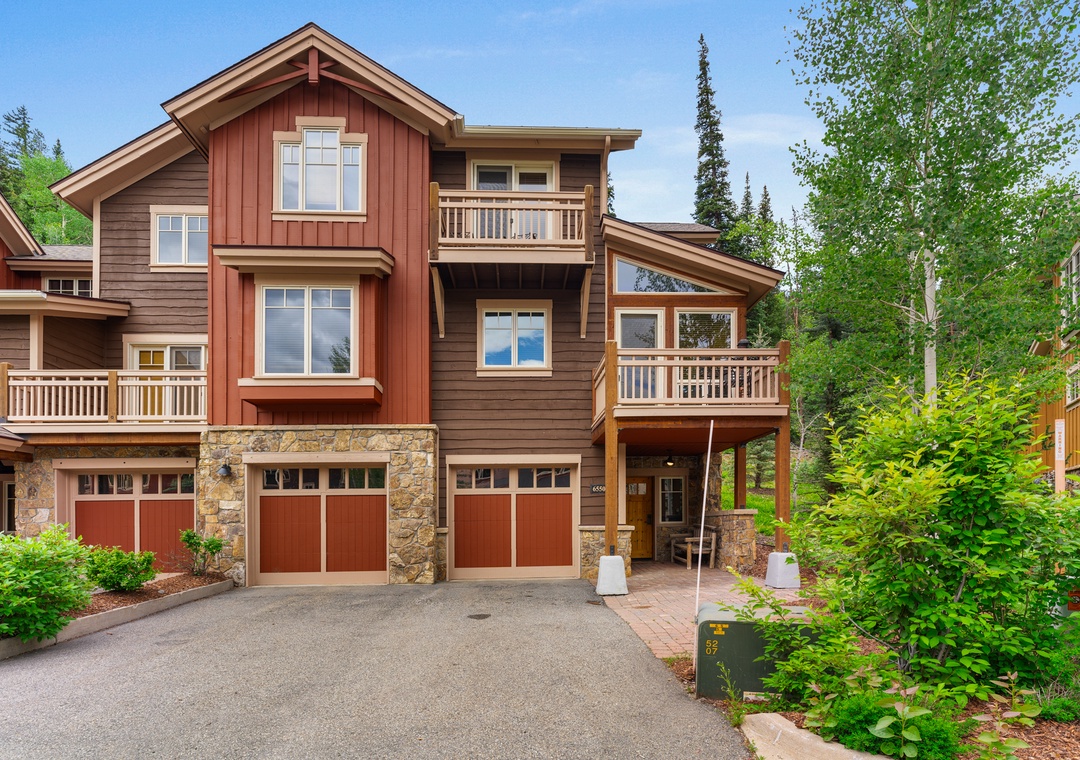 Mountain townhome with stone and wood facade, featuring private garage and forest backdrop.