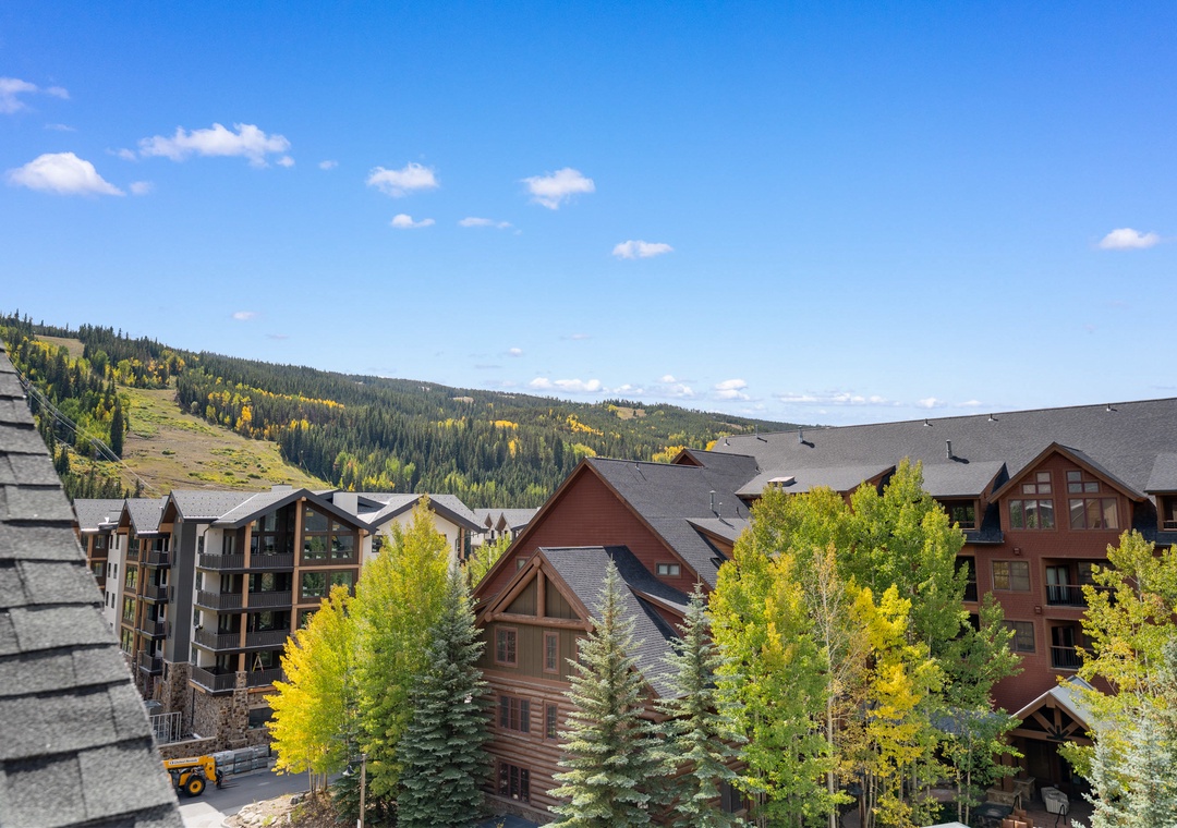 Mountain resort buildings nestled among colorful aspen trees with scenic alpine slopes in the background.