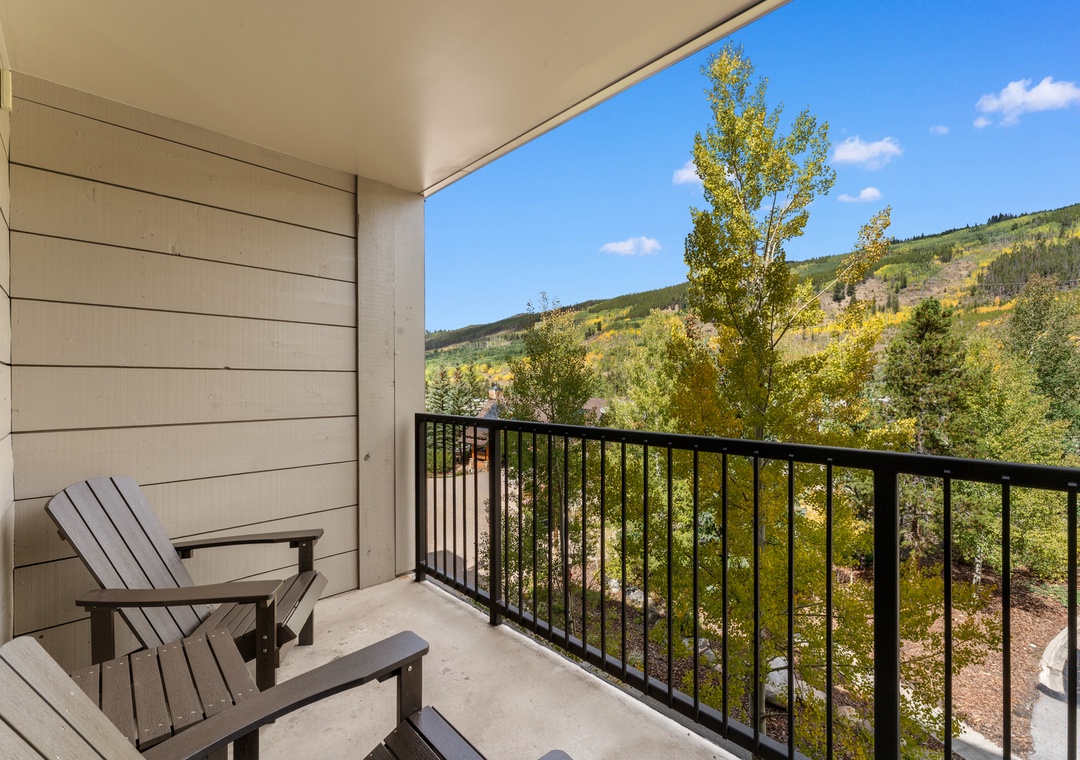 Stunning mountain landscape framed by vibrant autumn foliage visible from the private balcony, featuring comfortable Adirondack chairs for relaxation.