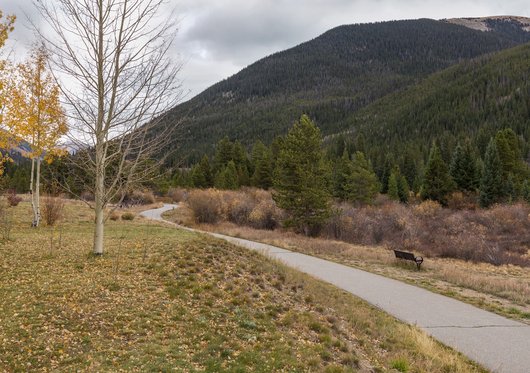 A peaceful walking trail winds through autumn landscapes beneath forested mountains in this scenic mountain valley setting.