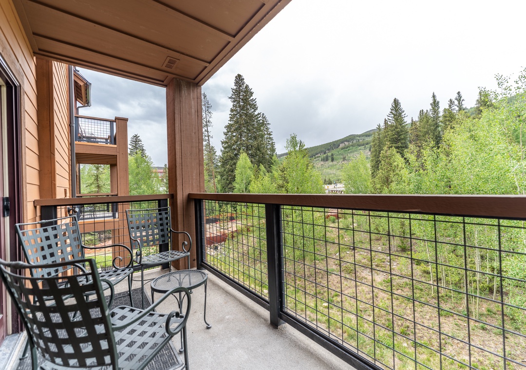 Your private balcony offers stunning mountain views through towering evergreens, with comfy seating for morning coffee or evening relaxation.