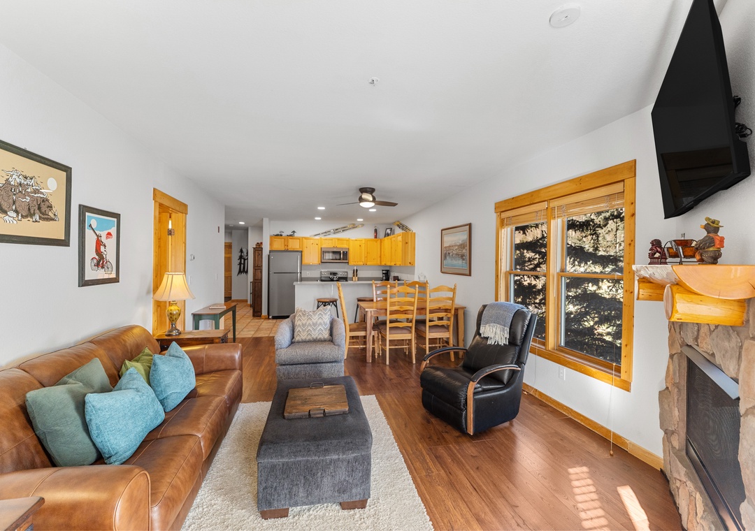 Relax in your open-concept living space featuring rich leather seating, a cozy fireplace, and stunning mountain views through oversized windows.