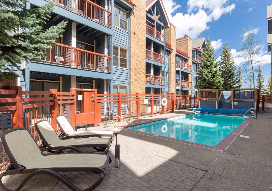 Multi-story apartment complex with swimming pool area surrounded by orange railings and lounge chairs.