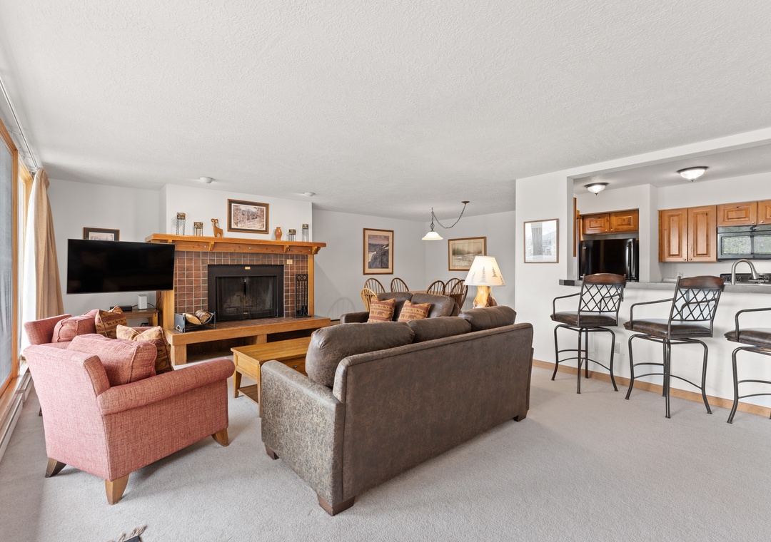 Relax in this inviting living space with a cozy fireplace, comfortable seating, and a fully-equipped kitchen perfect for preparing meals during your stay.