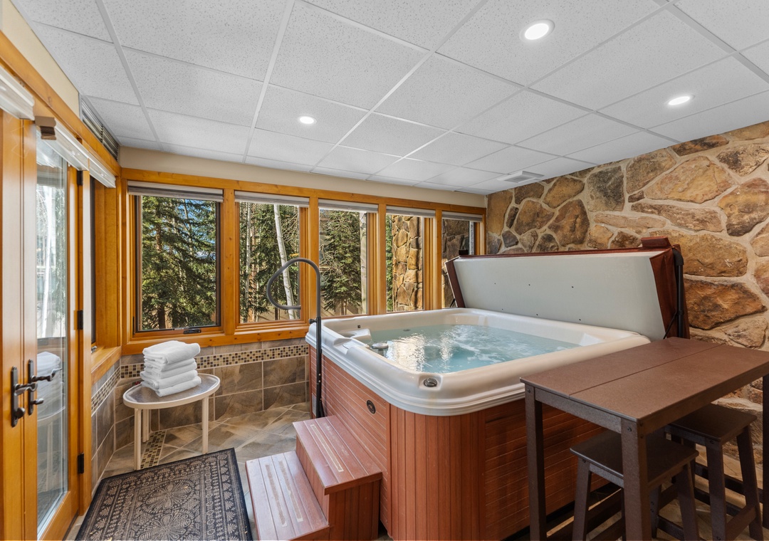 Unwind in your private hot tub surrounded by natural stone and panoramic forest views through floor-to-ceiling windows.