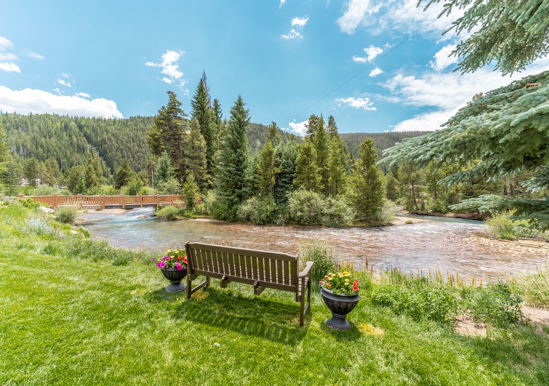Relax on your private riverside bench surrounded by vibrant flower planters, with the peaceful river and mountain forest creating the perfect backdrop for morning coffee or evening reflection.