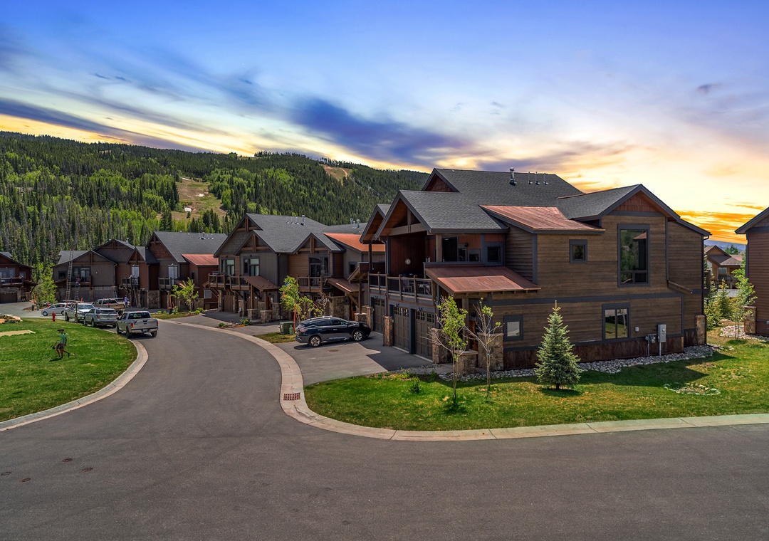 Modern mountain homes nestled in a scenic community with forested hillsides and vibrant sunset skies creating a peaceful alpine setting.
