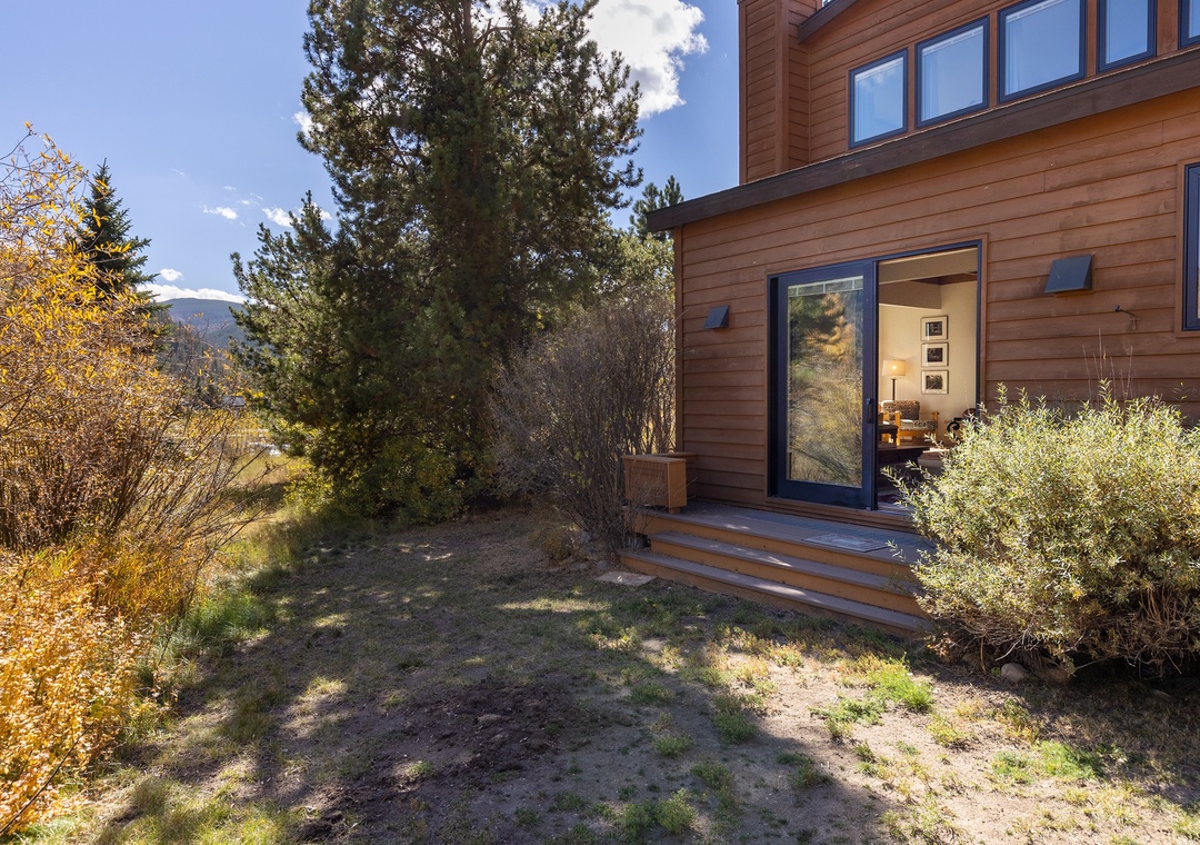 Modern mountain cabin nestled among mature trees with natural landscaping and mountain views in the distance.