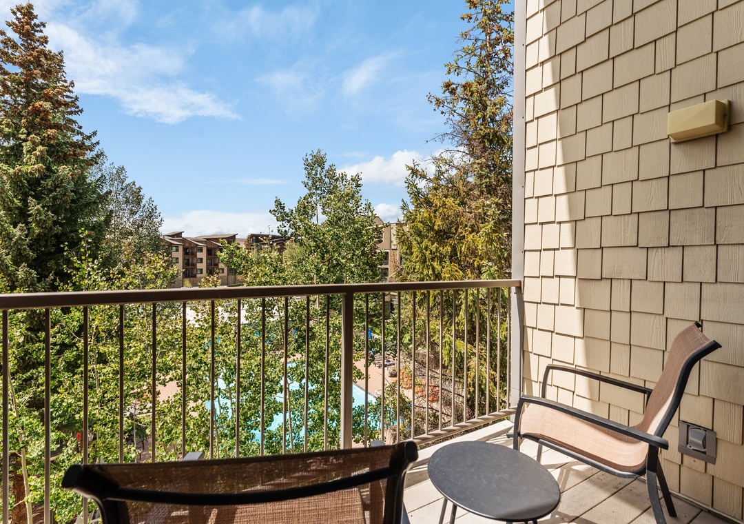 Step onto your private balcony and take in peaceful views of lush greenery and the sparkling pool below, framed by towering trees and blue skies overhead.