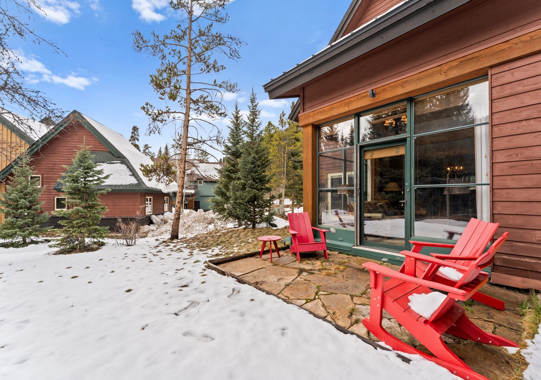 Step onto your private patio where bright red chairs invite cozy moments surrounded by snowy mountain serenity and towering pines.