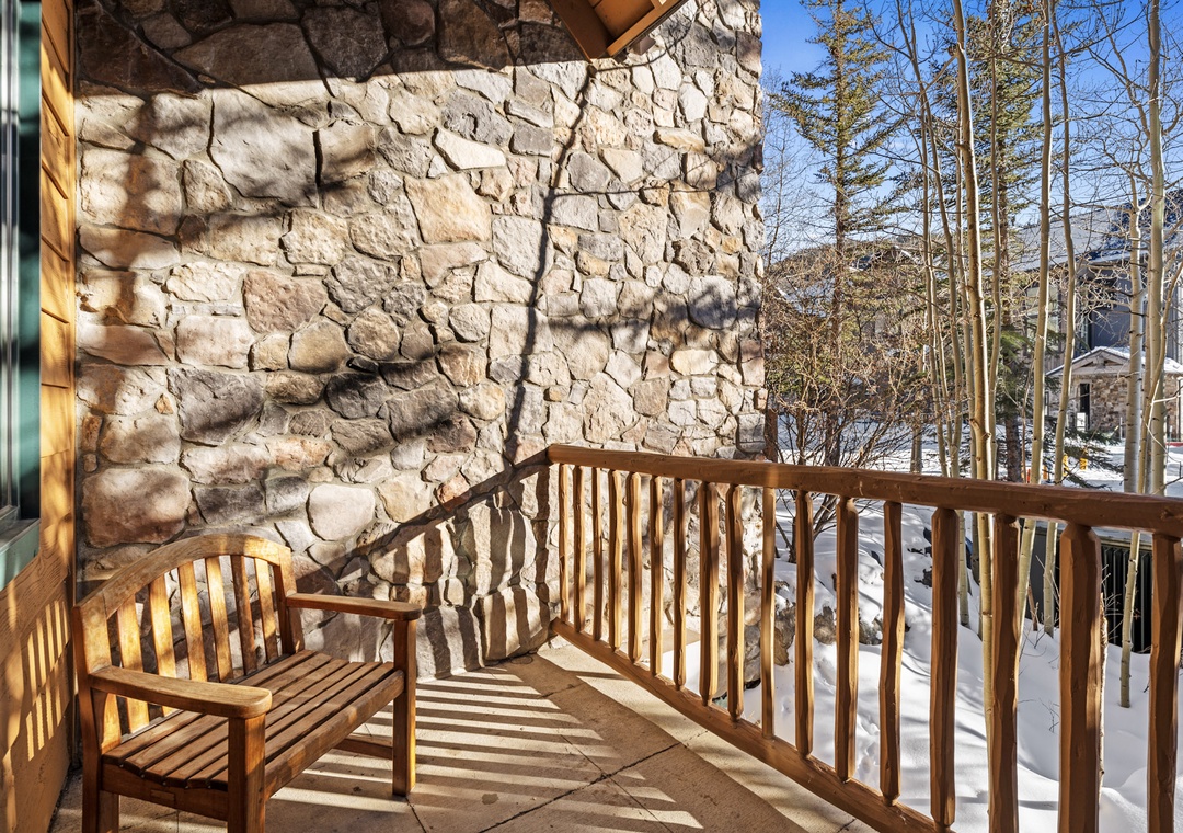 Rustic stone fireplace and wooden deck create a cozy mountain retreat setting surrounded by snow-covered trees.